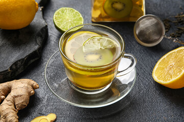 Glass cup of fruit tea with kiwi, lemon, lime and ginger on dark background, closeup