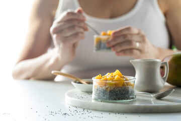 A close up view of a mango chia pudding snack with a woman eating one in behind.