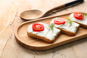 Wooden board of bread rusks with cream cheese and tomatoes on color background, closeup