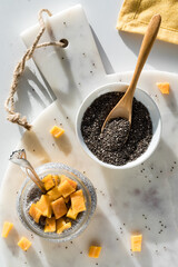 A mango chia pudding parfait on a marble board with a bowl of chia seeds.