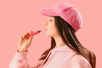 Young woman in cap with disposable electronic cigarette on pink background, closeup