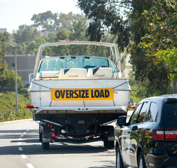 A large white motor boat being hauled on a trailer with a yellow sign stating Oversize Load