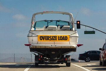 A large white motor boat being hauled on a trailer with a yellow sign stating Oversize Load