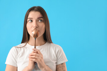 Thoughtful young woman with golden spoon on blue background