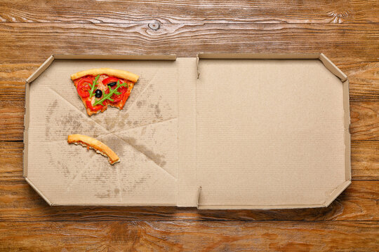 Pizza box with leftovers on wooden background