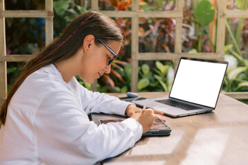 Woman designer with digital tablet and laptop computer in summer office