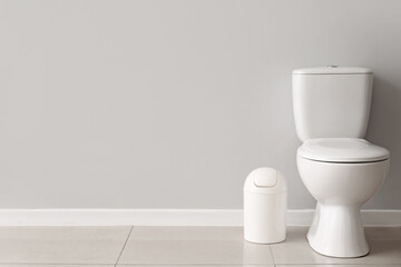 Ceramic toilet bowl and bin near grey wall