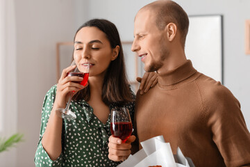 Young couple with bouquet of flowers drinking wine at home on Valentine's Day