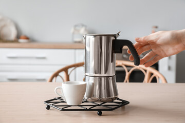Grid with geyser coffee maker and cup on table in kitchen