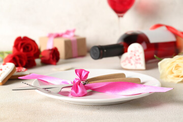 Obraz na płótnie Canvas Plate and cutlery tied with pink ribbon on light table. Valentine's Day celebration
