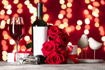 Glass of wine, bottle, rose flowers and gifts on table against blurred lights. Valentine's Day...
