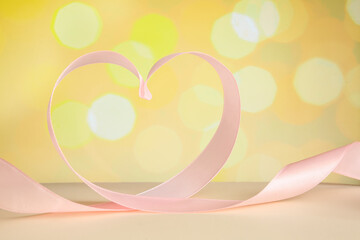 Heart made of pink satin ribbon on table against blurred lights