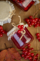 Fototapeta na wymiar Viburnum fruit jam in a glass jar on a wooden table near the ripe red viburnum berries. Source of natural vitamins. Used in folk medicine. Autumn harvest.