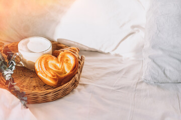 Obraz na płótnie Canvas Wicker tray with croissants and coffee on white bed linen.