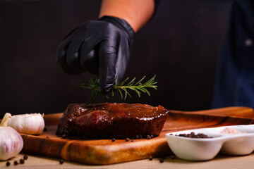 professional Chef hands cooking meat steak and adding rosemary leaf on black copy space background for menu restaurant or recipe text.