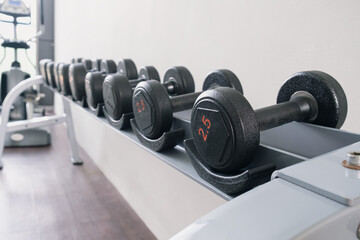 Black metal dumbbells of different weights on a rack in a gym. Sports equipment for increasing...