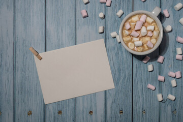 Empty greeting or invitation card mock up with white cup of coffee and marshmallows on wooden blue background. Blank paper copy space for your text. Valentines day, Happy fathers mothers day, Womens 