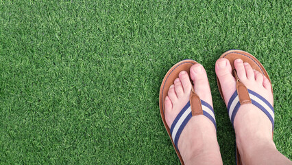 Female legs in flat leather sandals on a green artificial turf. The concept of summer holidays,...