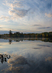 A dramatic sky reflected in the calm surface of a small Northwoods lake at sunrise.