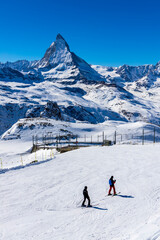 Two skiers on the way to ski slope in Swiss Alps in sunny day,Matterhorn behind. Small wooden house...