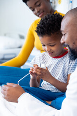 Vertical of african american male doctor showing inhaler to boy patient, with mother