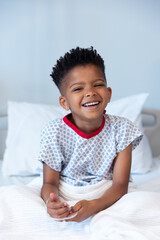 Happy african american boy patient sitting up in hospital bed, smiling with copy space