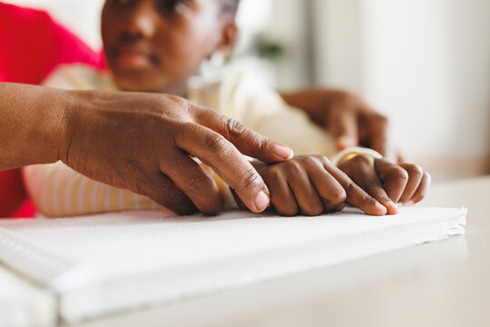 Happy african american grandmother and blind granddaughter reading braille - Powered by Adobe