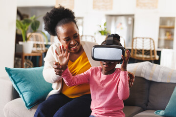 Happy african american grandmother and granddaughter using vr headset in living room