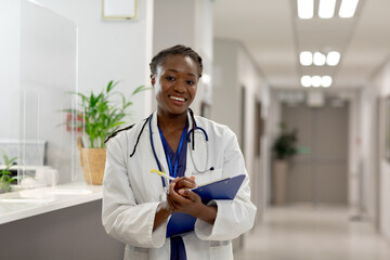 Portrait of happy african american female doctor working at hospital, holding clipboard
