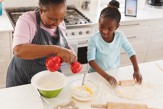 Happy african american grandmother and granddaughter baking together in kitchen