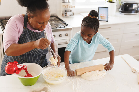 Happy african american grandmother and granddaughter baking together in kitchen