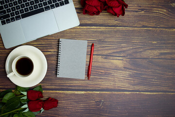 Working space with grey notebook, red roses and coffee over the wooden table. 