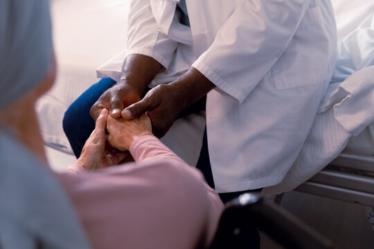 Close Up Of African American Doctor And Senior Caucasian Cancer Patient In Head Scarf Holding Hands