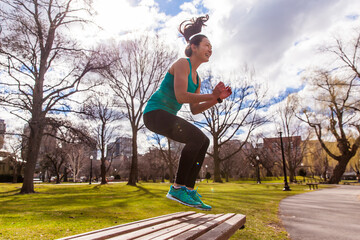Woman jumping while exercising on bench in park, Boston, Massachusetts, USA