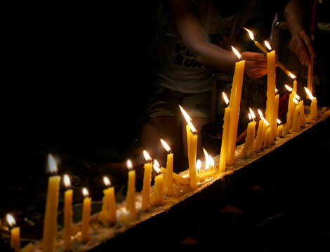 Burning candles and a worshiper holding incense to the flame
