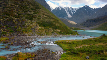 Fototapeta na wymiar The turquoise water of the Karakabak River flows from the lake among the stones in the Altai mountains.