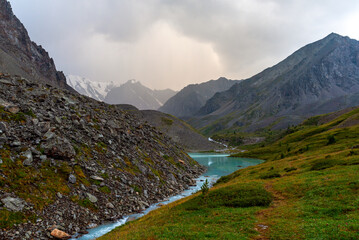 Fototapeta na wymiar The trail goes along the turquoise water of the Karakabak River flows out of the lake among the stones in the Altai mountains under thick clouds.