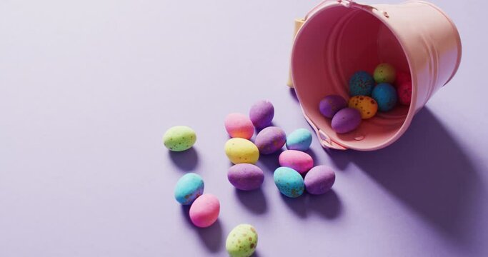 Bucket with colorful easter eggs on purple background with copy space