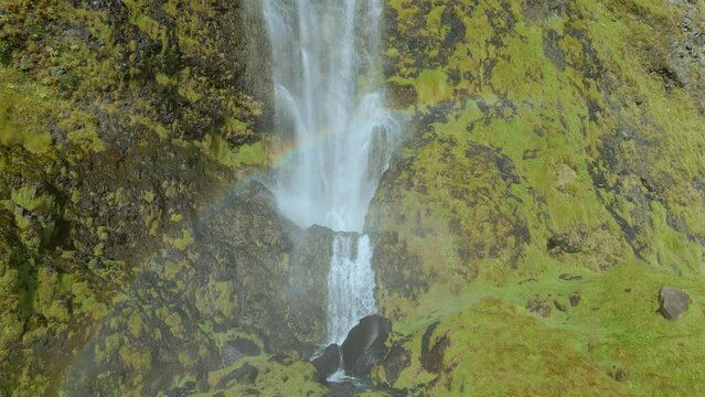 water cascading down a waterfall with a rainbow and green moss covering the rocky cliff face.