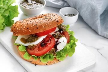 Sandwich, toast, bagel with mozzarella cheese, pesto sauce, tomatoes. Caprese Sandwich on white cutting board.
