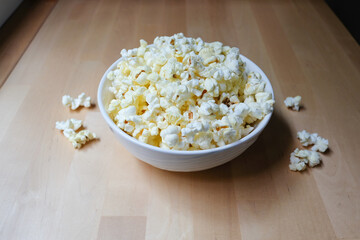 Popcorn snack in bowl on a light wood table. Pop corn ready to wath movie.