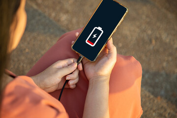 Close up a woman sitting on floor hands charging her smart phone with charging icon