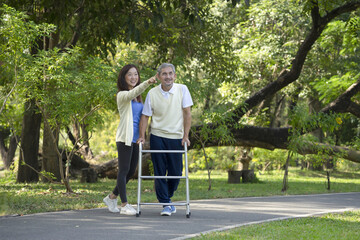 Fototapeta premium disabled senior man walking with walker, happy family, father and daughter enjoy talking and exercising in the public park, concept of daughter helps disabled father to exercise, elderly health care