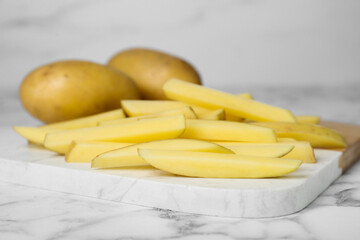 Whole and cut raw potatoes on white marble table, closeup. Cooking delicious French fries
