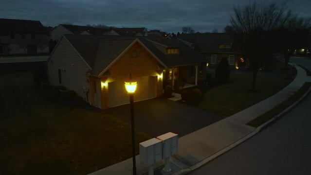 Aerial orbit around street light revealing small American home at night. Bright lamp with yellow hue.