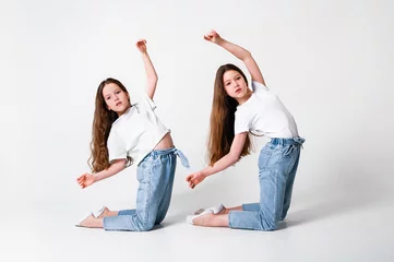 Poster teenagers girls in jeans and white t-shirts synchronously perform dance moves on a white background © Kiryakova Anna
