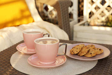 Cups with tasty cocoa and cookies on rattan table at balcony