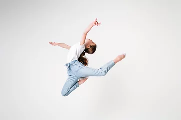 Fotobehang A teenage girl in jeans and a white T-shirt performs dance moves. White background © Kiryakova Anna