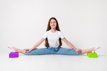 A teenage girl in jeans and a white t-shirt stretches her legs with green and purple styrofoam cubes. White background. The concept of sports, yoga.