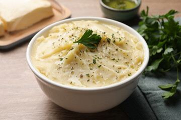 Bowl of delicious mashed potato with parsley on wooden table, closeup